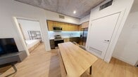 This contemporary 1180 square foot apartment offers a harmonious blend of urban living and natural elements. The space boasts five bedrooms, including an expansive 570 square foot primary bedroom, providing ample living quarters. Two well-appointed bathrooms serve the residence, ensuring comfort and convenience.

The apartment's design embraces a modern aesthetic with clean lines and a neutral color palette. Exposed concrete ceilings add an industrial touch, contrasting beautifully with the warm wooden floors throughout. Large windows in the bedrooms allow natural light to flood the space, while offering picturesque views of the surrounding greenery.

The kitchen is a standout feature, showcasing sleek wooden cabinetry, stainless steel appliances, and under-cabinet lighting that creates a warm ambiance. A generous wooden dining table adjoins the kitchen, perfect for casual meals or entertaining.

Bedrooms are thoughtfully designed with built-in storage solutions and minimalist decor. The bathrooms feature glass-enclosed showers, modern fixtures, and ample counter space. An outdoor area with lush plantings provides a serene retreat from city life.

This apartment seamlessly combines functionality with style, offering a comfortable and sophisticated urban living experience in the heart of downtown.