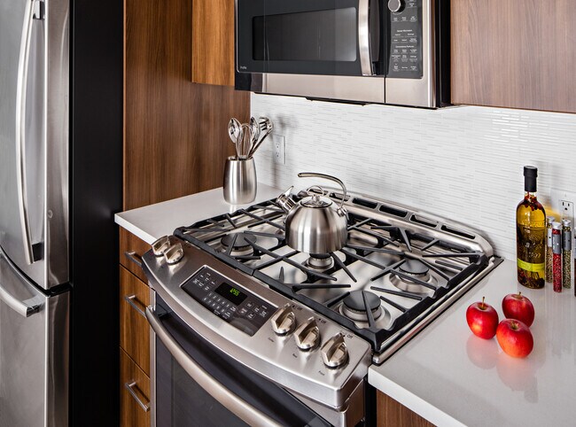 Cocina Signature Collection con gabinetes de roble, encimeras de cuarzo gris claro, protector contra salpicaduras de azulejos blancos, electrodomésticos de acero inoxidable renovados y pisos de tablones de superficie dura. - Avalon Princeton