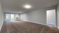 Located at 92 Fairhaven Blvd in Woodbury, NY, Unit 128 is a thoughtfully designed single-floor residence that balances comfort and functionality. The interior is finished with soft, neutral-toned carpet throughout the living and bedroom areas, complemented by cool gray walls and crisp white trim that create a clean, cohesive aesthetic.

The generously sized living area provides an open, airy feel with recessed and flush-mount lighting, a wall-unit air conditioner, and baseboard heating for year-round comfort. A door leads to an outdoor area, allowing natural light to fill the space. Multiple additional rooms offer flexible use as bedrooms or private spaces, each featuring windows that frame views of the surrounding greenery, wall-unit air conditioning, and baseboard heating.

The kitchen is a standout highlight, outfitted with white cabinetry, granite countertops, a subway tile backsplash, and a full suite of stainless steel appliances including a gas range, microwave, and dishwasher. The bathroom is equally well-finished, featuring white subway tile surrounding a soaking tub, a marble-topped vanity with brushed gold fixtures, and light wood-look tile flooring. This residence offers a move-in-ready environment with modern finishes throughout.