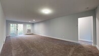 Located at 92 Fairhaven Blvd in Woodbury, NY, Unit 128 is a thoughtfully designed single-floor residence that balances comfort and functionality. The interior is finished with soft, neutral-toned carpet throughout the living and bedroom areas, complemented by cool gray walls and crisp white trim that create a clean, cohesive aesthetic.

The generously sized living area provides an open, airy feel with recessed and flush-mount lighting, a wall-unit air conditioner, and baseboard heating for year-round comfort. A door leads to an outdoor area, allowing natural light to fill the space. Multiple additional rooms offer flexible use as bedrooms or private spaces, each featuring windows that frame views of the surrounding greenery, wall-unit air conditioning, and baseboard heating.

The kitchen is a standout highlight, outfitted with white cabinetry, granite countertops, a subway tile backsplash, and a full suite of stainless steel appliances including a gas range, microwave, and dishwasher. The bathroom is equally well-finished, featuring white subway tile surrounding a soaking tub, a marble-topped vanity with brushed gold fixtures, and light wood-look tile flooring. This residence offers a move-in-ready environment with modern finishes throughout.