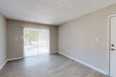 This single-floor residence offers a clean, neutral aesthetic throughout, making it a versatile and welcoming space. The open living area is finished with light wood-look luxury vinyl flooring that flows seamlessly through the main spaces, complemented by warm greige-toned walls and crisp white trim. A textured popcorn ceiling adds a classic touch overhead, while multiple HVAC vents ensure year-round comfort. Natural light pours in through a large sliding glass door fitted with vertical blinds, opening to an outdoor patio area framed by greenery — a standout feature of the main living space. A louvered bifold closet door near the entryway provides convenient built-in storage. The kitchen is equipped with white cabinetry, granite-patterned countertops, a black electric range with overhead ventilation hood, and stainless steel refrigerator, offering a practical and attractive cooking environment. The bathroom echoes the kitchen's style with a matching granite vanity countertop, a full tub-shower combo, and a large wall mirror. A walk-in closet with wire shelving connects to the bathroom, providing generous storage. Carpeted flooring in the closet area adds a soft contrast to the hard surface floors found throughout the rest of the home.