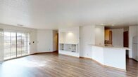 This single-floor residence offers a well-organized layout designed for comfortable everyday living. The open living area is finished with light wood-tone laminate flooring and features a built-in shelving unit, creating a practical focal point within the space. A sliding glass door floods the living room with natural light and provides direct outdoor access. The kitchen is equipped with warm oak cabinetry, a double-basin sink, a dishwasher, and a full-size refrigerator, with recessed lighting overhead and a peninsula that opens toward the living area for a connected feel. The bedrooms are carpeted and bright, each benefiting from large windows that invite ample natural light and views of the surrounding exterior. One bedroom features convenient direct access to the bathroom. The bathroom is thoughtfully appointed with a wide vanity topped with a light-colored countertop, wood cabinetry below, a large mirror with globe lighting, and a shower and tub combination enclosed by sliding frosted glass doors. Tile flooring completes the bathroom. Throughout the residence, warm wood-toned door and window trim provide a cohesive design element, while white walls keep the overall atmosphere clean and neutral.