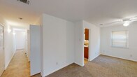 This single-story unit offers a straightforward, functional layout across multiple rooms connected by a clean, open flow. The living area is finished with neutral wall-to-wall carpeting and crisp white walls, creating a bright and adaptable space. A ceiling fan overhead and a window fitted with horizontal blinds provide both comfort and natural light. An adjacent carpeted room functions as an additional living or sleeping space, also featuring a window that allows natural light to filter in.

The kitchen is a standout feature of the unit, showcasing warm honey-toned oak cabinetry with ample upper and lower storage. Light laminate countertops line the perimeter, complemented by a double-basin stainless steel sink positioned beneath a window overlooking the outdoors. A white electric coil range and overhead exhaust fan complete the cooking area. A peninsula counter extends into the space, offering additional workspace and separation from the adjacent area. Tile flooring and crown molding add a finished touch. A sliding glass door provides direct outdoor access.

Two full bathrooms serve the unit, each featuring a full-size tub and shower combination, toilet, and vanity with a wood cabinet base. Tile flooring in both bathrooms adds durability, while the clean white fixtures maintain a consistent, neutral aesthetic throughout.