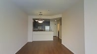 This single-floor residence offers a thoughtfully designed open-concept layout that seamlessly connects the living area to the kitchen. The space is anchored by rich, dark hardwood flooring that runs throughout, adding warmth and a sense of continuity to the interior.

The kitchen is a standout feature, equipped with sleek gray cabinetry, granite countertops, and stainless steel appliances including a refrigerator, microwave, and range. A peninsula-style breakfast bar separates the kitchen from the living area, making it ideal for casual dining or entertaining. A stylish pendant light hangs above the peninsula, providing focused task lighting while contributing to the modern aesthetic.

The walls are finished in a clean, neutral white, creating a bright and open atmosphere. Recessed lighting in the kitchen complements the pendant fixture, ensuring the space is well-lit. A hallway visible from the main living area leads to additional rooms, suggesting a practical and well-organized floor plan. The overall ambiance is contemporary and polished, with a minimalist design that allows the architectural details and quality finishes to take center stage throughout the space.