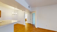 This single-floor residence offers a well-organized layout that balances functional living spaces with a clean, bright aesthetic throughout. The open-concept living area is finished with warm hardwood-style flooring that extends seamlessly through the main spaces, complemented by crisp white walls that enhance the sense of openness. A ceiling fan overhead adds to the comfort of the living room, which also features a sliding glass door that invites natural light and provides access to an outdoor area.

The kitchen is designed in a galley style, lined with warm-toned wood cabinetry on both sides offering generous storage. White appliances — including a gas range, microwave, dishwasher, and refrigerator — are neatly integrated alongside light countertops and a stainless steel sink. A peninsula counter opens the kitchen toward the dining area, which is accented by a decorative chandelier.

The hallway connects the main living spaces to the bedroom, which features plush carpeted flooring and ample wall space. A closet is conveniently located nearby. The bathroom is finished with light ceramic tile flooring, a wood-toned vanity with generous counter space, a full tub-and-shower combination with white tile surround, and a frosted window that allows natural light while maintaining privacy.