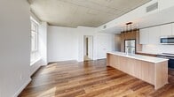 Located on the 11th floor in Portland's vibrant Pearl District, this two-bedroom, two-bathroom apartment offers a contemporary urban living experience defined by clean lines and modern industrial design. The open-concept living and kitchen area is anchored by rich hardwood flooring, exposed concrete ceilings, and floor-to-ceiling windows that frame panoramic views of the Portland skyline and surrounding cityscape. The kitchen is a standout feature, equipped with stainless steel appliances, a large waterfall-edge island with an undermount sink, warm wood cabinetry paired with white upper cabinets, and a striking pendant light fixture overhead. The living area flows seamlessly from the kitchen, bathed in abundant natural light from expansive windows on multiple walls. Both bedrooms offer plush carpeting, sliding closet doors, and city views, with the primary bedroom providing a generous layout. Each bathroom is finished with wood-toned vanity cabinetry, clean white countertops, and bright lighting. One bathroom features a walk-in shower, while the second includes a full soaking tub. Throughout, the design balances industrial elements with warm finishes, creating a refined and cohesive aesthetic suited for modern urban living.