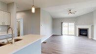 This single-floor home on Captains Way in North Tonawanda, NY, presents a clean, modern design with a thoughtfully arranged open-concept floor plan. The main living and dining area flows seamlessly from the kitchen, unified by durable wood-look flooring and soft gray walls throughout. Vaulted ceilings rise over the living space, enhancing the sense of openness, while a ceiling fan provides both comfort and style. Sliding glass doors along one wall flood the area with natural light and offer views of the surrounding greenery.

The kitchen is well-appointed with white shaker-style cabinetry, light quartz countertops, stainless steel appliances including a gas range, microwave, and refrigerator, and a peninsula with a built-in sink — ideal for both cooking and casual dining. A pendant light fixture adds a contemporary accent above the workspace.

The bedrooms feature plush carpeting and windows that frame outdoor views, creating bright and comfortable retreats. The bathroom is finished with a white vanity, quartz countertop, large mirror with lighted surround, and wood-look flooring. The attached two-car garage offers generous vehicle storage with an automatic opener already in place.