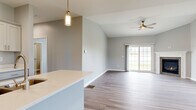 This single-floor home on Captains Way in North Tonawanda, NY, presents a clean, modern design with a thoughtfully arranged open-concept floor plan. The main living and dining area flows seamlessly from the kitchen, unified by durable wood-look flooring and soft gray walls throughout. Vaulted ceilings rise over the living space, enhancing the sense of openness, while a ceiling fan provides both comfort and style. Sliding glass doors along one wall flood the area with natural light and offer views of the surrounding greenery.

The kitchen is well-appointed with white shaker-style cabinetry, light quartz countertops, stainless steel appliances including a gas range, microwave, and refrigerator, and a peninsula with a built-in sink — ideal for both cooking and casual dining. A pendant light fixture adds a contemporary accent above the workspace.

The bedrooms feature plush carpeting and windows that frame outdoor views, creating bright and comfortable retreats. The bathroom is finished with a white vanity, quartz countertop, large mirror with lighted surround, and wood-look flooring. The attached two-car garage offers generous vehicle storage with an automatic opener already in place.