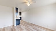 Located at 1231 Persimmon Avenue in El Cajon, California, this efficient single-floor, one-bedroom, one-bathroom unit offers a thoughtfully arranged layout that maximizes every inch of its compact footprint. Light wood-tone flooring runs throughout the entire space, lending warmth and visual continuity from room to room.

The open-concept living, dining, and kitchen area forms the heart of the unit. A ceiling fan provides year-round comfort, while a large window dressed with vertical blinds welcomes an abundance of natural light and neighborhood views. The kitchen features bold navy cabinetry with a contrasting light countertop and a peninsula that neatly delineates the cooking space from the living area.

The bedroom is a comfortable, well-proportioned retreat bathed in natural light from a large window. A wall-mounted air conditioning unit ensures climate control, and an open closet with dual wire shelving tiers offers generous storage, framed by dramatic dark curtain panels.

The bathroom is clean and functional, equipped with a shower-tub combination featuring a handheld showerhead and safety grab bar, alongside a toilet and a built-in shelving nook for added convenience.

Throughout the unit, crisp white walls and consistent flooring create a bright, cohesive ambiance that feels open and move-in ready.
