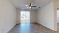This single-story residence is designed with a clean, contemporary aesthetic that flows consistently throughout. The open-concept living area is finished with light hardwood-style flooring and neutral white walls, creating a bright and airy atmosphere. A ceiling fan overhead adds comfort, while a sliding glass door fitted with vertical blinds opens to an outdoor space, allowing natural light to fill the room.

The kitchen is a standout feature, showcasing a central island with granite countertops and pendant lighting above. Dark espresso cabinetry is paired with white upper cabinets and complemented by a tiled backsplash. Stainless steel appliances, including a refrigerator, range, microwave, and dishwasher, are fully integrated. A dedicated pantry with built-in shelving provides ample storage.

The additional rooms continue the light hardwood-style flooring and are brightened by windows with horizontal blinds. The bathroom features a double vanity with granite countertops, white cabinetry, a large mirror, and a glass-enclosed shower, maintaining the modern, polished feel found throughout the rest of the space.