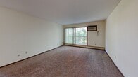 Located at 3359 Coachman Rd in Eagan, MN, this 2-bedroom, 1-bathroom residence offers a functional and comfortable single-floor layout. The living room is generously sized, featuring plush carpeting, a large sliding glass door that opens to a private balcony with tree-lined views, and a wall-mounted air conditioning unit. Natural light fills the space through vertical blinds, creating a bright and welcoming atmosphere. The kitchen is efficiently designed with rich dark cabinetry, granite-style countertops, light wood-look flooring, and black appliances including an electric range, over-the-range microwave, and refrigerator — offering ample storage and functionality. Both bedrooms are carpeted and feature neutral walls, vertical blind-covered windows, baseboard heating, and louvered bi-fold closet doors, providing comfortable and practical personal spaces. The primary bedroom is well-proportioned with generous closet storage. The full bathroom includes a tub/shower combination, a dark wood vanity with a white countertop, a mirror, and light wood-look flooring. Throughout the residence, dark wood-trimmed doors and textured ceilings add a consistent design element, while the overall layout ensures easy flow between all rooms.
