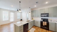 Located at 1000 E Yager Ln in Austin, TX, this well-appointed two-bedroom, two-bathroom residence offers a thoughtfully designed single-floor layout with modern finishes throughout. Warm wood-look flooring flows seamlessly across the entire space, creating a cohesive and inviting atmosphere.

The kitchen serves as a central highlight, featuring sage-green cabinetry with brushed gold hardware, granite-look countertops, a central island with an undermount sink, and black appliances including a range, microwave, and refrigerator. Stylish globe pendant lights hang above the island, complementing the recessed ceiling lighting. White subway tile backsplash adds a clean, contemporary touch, while open shelving provides additional display space.

The open-concept layout connects the kitchen directly to the living area, which benefits from multiple windows and a ceiling fan, allowing for excellent natural light. The primary bedroom is a comfortable retreat with a walk-in closet and an en-suite bathroom featuring sage-green vanity cabinetry, granite countertops, and a glass-enclosed shower. The secondary bedroom includes dual windows and a ceiling fan. The second bathroom offers a tub-shower combination with white tile surround. The overall aesthetic is clean, modern, and move-in ready.