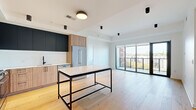 This contemporary single-floor residence showcases a thoughtfully designed open-concept layout with consistent light hardwood flooring throughout. The kitchen serves as a central highlight, combining warm wood lower cabinetry with deep navy upper cabinets, white subway tile backsplash, stainless steel appliances including a gas range, microwave, and French door refrigerator, and a striking marble-topped island with a black metal frame — ideal for both meal preparation and casual dining.

The living area extends seamlessly from the kitchen toward floor-to-ceiling sliding glass doors that open to a private balcony, flooding the space with natural light and offering elevated city views. Additional bedrooms feature large black-framed windows with similar urban vistas and well-sized closets with built-in rods.

Two bathrooms provide distinct design approaches: one features geometric black-and-white patterned floor tile, white subway-tiled tub surround, and matte black fixtures, while the primary bath offers a frameless glass walk-in shower with large-format stone-look tile, a double-sink white quartz vanity atop a wood and black metal base, and matte black hardware throughout. The overall aesthetic is clean, modern, and cohesive.