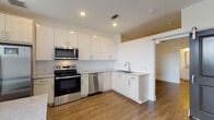 Located at 44 Braves Ave in Lawrenceville, Georgia, this single-floor unit offers a clean, contemporary design throughout. The layout is efficiently organized, beginning with a bright, narrow entryway hallway featuring crisp white walls, wood-look flooring, and a glass-paneled exterior door that draws in natural light. An electrical panel is conveniently recessed into the hallway wall, and a louvered interior door adds a stylish touch near the entrance.

The kitchen is a standout feature, outfitted with a full suite of stainless steel appliances including a French door refrigerator with ice maker, electric range, over-the-range microwave, and dishwasher. White shaker-style cabinetry extends to the ceiling, providing generous storage, while a classic white subway tile backsplash and light stone countertops complete the polished look. Wood-look flooring flows seamlessly throughout, and a ceiling fan with light keeps the space comfortable. A glass balcony door floods the kitchen with natural light and provides outdoor access.

The living area is open and versatile, featuring the same wood-look flooring, a ceiling fan, and a clerestory window that allows additional light into the space. The bathroom includes a full tub-shower combination with white subway tile surround and chrome fixtures. The overall aesthetic is modern, clean, and move-in ready, making this a well-appointed and functional single-level space.