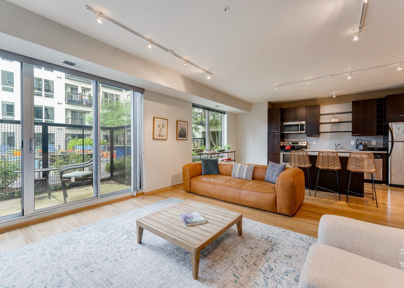 Modern living room with a tan sofa, coffee table, and open kitchen with island seating.