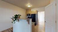 Located at 165 McBride St in Saint Helens, Oregon, this single-story unit offers a thoughtfully designed open layout with consistent wood-look flooring flowing throughout. The kitchen serves as a central feature, anchored by a peninsula with speckled granite countertops that provide both prep space and a casual breakfast bar. Warm-toned wood cabinetry extends to the upper walls for ample storage, while black appliances — including a refrigerator, range, microwave, and dishwasher — lend a cohesive, modern look. A double-basin sink sits conveniently within the peninsula.

The open-concept design connects the kitchen seamlessly to the living area, which benefits from natural light through multiple windows and a ceiling fan with light fixture overhead. A wall-mounted HVAC unit provides climate control. The living space is generously proportioned, offering flexibility for various furniture arrangements.

A dedicated room features a built-in murphy bed with integrated shelving, maximizing functionality without sacrificing floor space, along with a door providing access to natural light. The bathroom is clean and bright, finished with hexagonal tile flooring, a shower with a curtain rod, and crisp white walls and fixtures throughout. The overall ambiance is fresh, practical, and move-in ready.