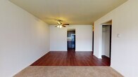 Located at 321 W Dayton-Yellow Springs Rd in Fairborn, Ohio, this single-floor unit offers a practical and well-appointed layout. The main living area makes a strong impression with rich, dark hardwood-style flooring that extends toward the kitchen, complemented by a ceiling fan with light fixture that provides both comfort and illumination. A natural transition leads into a carpeted area, adding warmth and a clear distinction between living and sleeping zones.

The kitchen is efficiently designed with dark espresso-toned cabinetry, light granite-style countertops, a stainless steel sink, and black appliances including an electric range with overhead ventilation. Ample upper and lower cabinet storage makes the space highly functional.

The bedrooms feature neutral-toned carpet, white walls, and windows with blinds that allow for natural light while maintaining privacy. One bedroom includes a wall-mounted air conditioning unit and a baseboard heater, offering year-round climate control. A closet is visible off the main living area, providing additional storage.

The bathroom is elongated and well-equipped, featuring the same hardwood-style flooring, a wide vanity with granite-style countertops and dark cabinetry, and a full tub and shower combination. Overall, the unit presents a cohesive, neutral palette with dark accents throughout.