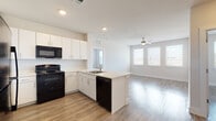 This thoughtfully designed single-floor residence offers a clean, contemporary aesthetic with an open-concept layout that seamlessly connects the kitchen and living area. The kitchen is well-appointed with crisp white cabinetry extending to the ceiling for ample storage, a peninsula island with an integrated sink, light-toned countertops, and black appliances including a gas range, over-the-range microwave, dishwasher, and full-size refrigerator. Light wood-look flooring runs consistently throughout the space, enhancing the bright and airy feel. The open living area benefits from multiple windows that invite generous natural light, and is equipped with a ceiling fan for added comfort. Bedrooms are generously proportioned, each featuring the same wood-look flooring, neutral wall tones, and windows with exterior views. Both bathrooms maintain a consistent, clean design with white tile tub-and-shower surrounds, white vanities with light countertops, and wood-look flooring that ties the space together. The overall ambiance is modern and move-in ready, characterized by a neutral palette, recessed lighting, and a cohesive design language that flows naturally from room to room.