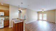 Located in Snellville, GA, this one-bedroom, one-bathroom unit offers a thoughtfully designed single-floor layout that maximizes every square foot. The open-concept living and kitchen area is finished with warm wood-look flooring and neutral beige walls, creating a bright and welcoming atmosphere. A ceiling fan with a light fixture keeps the space comfortable, while French doors flood the living area with natural light and provide access to the outdoors. The kitchen is well-equipped with rich wood cabinetry, granite-style countertops, recessed lighting, and white appliances including a refrigerator, electric range, and over-the-range microwave. A dedicated closet off the kitchen provides additional storage. The bedroom is a comfortable retreat featuring plush carpeting, a ceiling fan, and multiple windows that invite natural light and outdoor views. A dedicated closet adds practical storage. The bathroom is finished with tile flooring, a wood-toned vanity with a granite-style countertop, a large mirror with overhead lighting, and a walk-in shower. Clean, neutral tones carry throughout the home, offering a move-in-ready canvas with a functional and cohesive design.