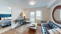 Located at 21400 International Blvd in SeaTac, Washington, this single-floor residential unit offers a thoughtfully designed open-concept layout finished with warm hardwood-style flooring throughout the main living areas. The kitchen is a functional centerpiece, equipped with dark espresso cabinetry, black appliances including a range, microwave, dishwasher, and refrigerator, as well as light countertops that provide a clean contrast. A freestanding island with a butcher block top and seating offers additional prep space and a casual dining option, enhancing the kitchen's practicality.

The kitchen flows seamlessly into the living area, which is bright and welcoming, benefiting from natural light through a glass door that opens directly onto a private balcony with outdoor views. The living space is well-proportioned and versatile, providing ample room for varied furniture arrangements.

The bedroom is a comfortable retreat featuring plush carpet, multiple windows that invite natural light and outdoor views, and generous space for furnishings. The bathroom includes hardwood-style flooring, clean white fixtures, and a shower-tub combination. The overall aesthetic throughout the unit is modern and neutral, creating a cohesive and inviting atmosphere.
