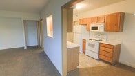 This single-floor residence presents a practical and well-organized layout, highlighted by a central hallway that connects the main living areas. The hallway is finished with neutral-toned carpet and features distinctive built-in wall niches, adding subtle architectural interest to the corridor. These recessed details provide visual breaks along the walls and offer display space.

The kitchen is accessible directly from the hallway through a defined doorway, creating a clear separation between spaces. It is equipped with white appliances, including a refrigerator, electric range, and over-the-range microwave. Medium-toned oak cabinetry lines the walls, providing ample storage, while a peninsula with a light-colored countertop extends into the space, offering additional workspace and serving as a natural divider. The kitchen floor is finished with light-toned tile, contrasting with the carpeted areas elsewhere in the unit.

The hallway extends toward additional rooms at the rear, suggesting further living or sleeping spaces beyond what is immediately visible. The overall aesthetic is clean and functional, with neutral wall tones, textured ceilings, and consistent wood-toned accents throughout.