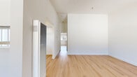 Located at 13628 Kornblum Ave in Hawthorne, California, this single-story, one-bedroom, one-bathroom residence offers a clean, modern aesthetic defined by crisp white walls and warm light wood flooring that runs consistently throughout the space. The open layout connects the living room and kitchen area, creating a cohesive and functional living environment. Natural light filters through windows fitted with vertical blinds in the living area, which also features a ceiling fan with a light fixture overhead and a wall-mounted heater unit. The U-shaped kitchen is well-appointed with white cabinetry extending to the ceiling, white countertops, a gas range, dishwasher, and a window above the sink that brings in additional natural light. A tray ceiling detail adds subtle architectural interest to the kitchen. The generously sized bedroom continues the light wood flooring and maintains the clean, neutral palette, with a window allowing natural light in. The bedroom includes a dedicated closet fitted with white shelving rods and sliding doors, offering practical storage. The bathroom features light wood-style flooring, a floating white vanity with built-in drawers, a toilet, and a full tub-shower combination, maintaining the unit's consistent minimalist, modern style throughout.
