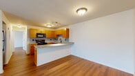 This single-floor unit is designed with a practical, open-concept layout that connects the kitchen and living areas seamlessly. The kitchen is a standout feature, outfitted with warm honey-toned wood cabinetry, granite countertops, and a coordinating tile backsplash in a speckled grey pattern. Black appliances, including an electric range with overhead microwave, are paired with a peninsula that doubles as a breakfast bar, creating a natural divide between the kitchen and the adjacent living space. Track lighting above the kitchen and flush-mount ceiling fixtures throughout provide consistent illumination across the unit.

The living area is generously proportioned, featuring rich hardwood-style flooring that runs throughout the entire unit, lending warmth and visual continuity. A sliding glass door allows natural light to pour in and provides access to an outdoor area. The bedroom is a comfortable, well-lit space with a large window offering exterior views of surrounding greenery and neighboring buildings. It features direct access to a walk-in closet fitted with wire shelving, as well as an adjoining bathroom. The bathroom includes a full-surround soaking tub and shower combination, finished in clean white.