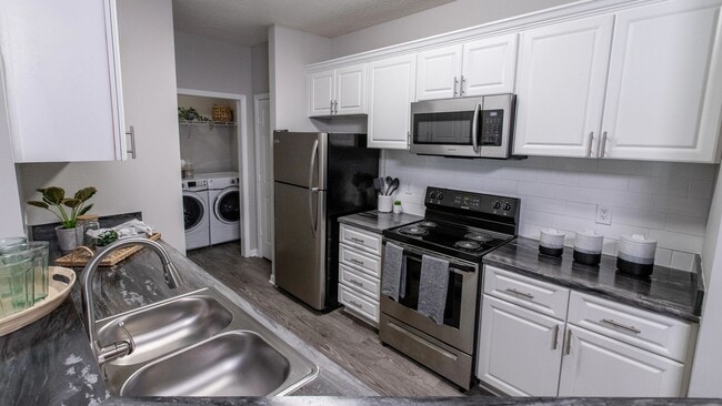 Experience timeless elegance in our updated kitchens, featuring white cabinetry, a modern subway tile backsplash, and wood-style flooring with stainless-steel appliances. - The Everlee Apartments
