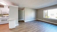 Located at 3460-3480 Carter Dr in South San Francisco, CA, this one-bedroom, one-bathroom unit offers a practical and well-appointed layout across a single floor. The open-concept living room and kitchen area forms the heart of the unit, with warm wood-look vinyl plank flooring running throughout and neutral taupe-toned walls that create a clean, cohesive look. A ceiling fan anchors the living room, while natural light filters in through windows. The kitchen is efficiently designed in a galley-style configuration, featuring white cabinetry with ample storage, a gas range with over-the-range microwave, a full-size refrigerator, and a double-basin stainless steel sink — all set against light countertops and matching white finishes. The bedroom is a comfortable size, enhanced by a large window that brings in natural light and outdoor views of surrounding greenery. Two closets provide generous storage, one of which is a walk-in style with wire shelving. The bathroom includes a full tub and shower combination with a curved curtain rod, a white vanity with stone-look countertop, and wood-look flooring consistent with the rest of the unit. Textured ceilings are featured throughout, adding dimension to the overall interior.