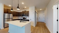 Located in Sugar Hill, GA, this Cadence Type A6 residence is a single-story, 1-bedroom, 1-bathroom home designed with modern living in mind. The open-concept layout connects the kitchen, dining, and living areas seamlessly, creating a bright and functional space. The kitchen is a standout feature, showcasing rich dark cabinetry, a subway tile backsplash, stainless steel appliances, recessed lighting, and a large white quartz island with an undermount sink and stylish pendant lighting overhead. Durable wood-look flooring runs throughout the main living areas, while a distinctive sliding barn door adds a contemporary architectural touch. The spacious bedroom features plush carpeting, a ceiling fan, and generous natural light through large windows with blinds. The bathroom is thoughtfully designed with dual undermount sinks, granite countertops, dark cabinetry, matte black fixtures, a tiled tub/shower combination, and wood-look flooring. Throughout the home, clean white walls, modern panel doors, and consistent dark hardware create a cohesive, contemporary aesthetic. The layout flows naturally from entry to living spaces, offering a comfortable and well-organized home in the Cadence community.