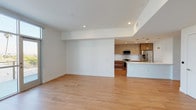 This single-floor unit showcases a clean, contemporary design with an open-concept layout that seamlessly connects the living area to the kitchen. Light hardwood flooring extends throughout the main living spaces, complemented by recessed lighting and crisp white walls that enhance the bright, airy atmosphere. A glass door opens to an outdoor balcony, inviting natural light and outdoor views into the living area.

The kitchen is well-appointed with two-tone cabinetry featuring warm wood lower drawers and matte upper cabinets, white quartz countertops, a geometric hexagonal tile backsplash, and a full suite of stainless steel appliances including a gas range, over-the-range microwave, and French door refrigerator. A center island with an integrated sink adds both workspace and casual dining potential.

The bedrooms are finished with plush carpet and feature large windows that frame neighborhood views, including glimpses of palm trees. The primary bedroom benefits from direct balcony access. A generously sized walk-in closet offers multiple hanging rods and adjustable shelving. The bathroom includes a frameless glass-enclosed walk-in shower with large-format tile surround and a mosaic tile floor. A stacked washer and dryer unit is conveniently housed within the unit.