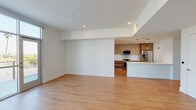 This single-floor unit showcases a clean, contemporary design with an open-concept layout that seamlessly connects the living area to the kitchen. Light hardwood flooring extends throughout the main living spaces, complemented by recessed lighting and crisp white walls that enhance the bright, airy atmosphere. A glass door opens to an outdoor balcony, inviting natural light and outdoor views into the living area.

The kitchen is well-appointed with two-tone cabinetry featuring warm wood lower drawers and matte upper cabinets, white quartz countertops, a geometric hexagonal tile backsplash, and a full suite of stainless steel appliances including a gas range, over-the-range microwave, and French door refrigerator. A center island with an integrated sink adds both workspace and casual dining potential.

The bedrooms are finished with plush carpet and feature large windows that frame neighborhood views, including glimpses of palm trees. The primary bedroom benefits from direct balcony access. A generously sized walk-in closet offers multiple hanging rods and adjustable shelving. The bathroom includes a frameless glass-enclosed walk-in shower with large-format tile surround and a mosaic tile floor. A stacked washer and dryer unit is conveniently housed within the unit.