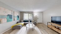 Located at 1250 Woodcrest Dr in Daytona Beach, FL, this one-bedroom residence offers a thoughtfully designed single-floor layout that maximizes every inch of its footprint. The open-concept living area features warm wood-look flooring, neutral gray walls, and a textured ceiling, creating a bright and welcoming atmosphere. A large window fitted with vertical blinds and patterned curtains allows generous natural light to fill the space, enhancing its airy feel.

The kitchen is positioned off the main living area and features white cabinetry, a stainless steel refrigerator, a gas range, and a granite-topped breakfast bar with barstool seating — ideal for casual dining or working from home. A dedicated nook adjacent to the kitchen accommodates a compact desk setup, adding functional versatility to the living zone.

The bedroom is carpeted and comfortably sized, with a bold yellow accent wall serving as a striking focal point. Sliding glass doors provide access to an outdoor area and invite additional natural light. A dedicated closet completes the bedroom's layout.

Throughout the space, cohesive neutral tones are accented with pops of yellow and teal, lending a modern, curated aesthetic. The overall design balances practicality with style, making this Daytona Beach residence a functional and attractive living option.