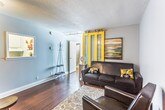 This 1-bedroom, 1-bathroom unit offers a cohesive and functional layout spread across a single floor. Rich hardwood flooring runs throughout, tying the space together with warmth and continuity.

The living area is a standout, anchored by a striking yellow-framed sliding barn door with frosted glass panels — a bold design choice that serves as a focal point while also offering flexible room division. Track lighting overhead adds an industrial touch, while soft gray walls create a neutral, calming backdrop. A pass-through window connects the living area to the kitchen, enhancing the open feel of the space.

The bedroom is comfortably sized, featuring the same warm hardwood floors and soft gray walls. A window allows natural light to filter in, brightening the room throughout the day.

The bathroom is clean and well-finished, with a white vanity offering ample cabinet storage, a well-lit mirror with overhead lighting, and a mosaic tile accent border that adds a decorative detail. The bathroom also benefits from an adjacent closet with a bifold door, providing convenient storage with a full hanging rod and shelving.

Overall, the unit delivers a stylish and practical living environment, with consistent finishes and thoughtful design details that make efficient use of the available space.