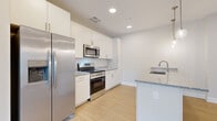 Located at 9606 Lamont Ave in Cleveland, OH, this 2-bedroom, 2-bathroom single-floor residence offers a clean, modern design with thoughtful finishes throughout. The open-concept layout connects the kitchen and living area, creating a bright and functional space illuminated by recessed lighting and stylish globe pendant lights. The kitchen is well-appointed with white shaker-style cabinetry, granite countertops, a central island with an integrated sink, and a full suite of stainless steel appliances, including a refrigerator, electric range, and microwave. Light wood-look flooring runs through the main living areas, contributing to a fresh and contemporary atmosphere. The primary bedroom offers comfortable proportions and is complemented by a walk-in closet with wire shelving for ample storage. Both bedrooms feature plush carpet flooring and neutral wall tones. The two bathrooms are finished with modern white vanities, sleek hardware, and wood-look flooring. A dedicated hallway connects the rooms efficiently. The unit's clean, neutral palette and modern fixtures create a cohesive and move-in-ready living environment well-suited for everyday comfort.