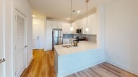 This well-appointed 2-bedroom, 2-bathroom residence at 523 N Spring St in Greensboro, NC offers a thoughtfully designed single-floor layout with modern finishes throughout. The open-concept living, dining, and kitchen area serves as the heart of the home, featuring warm hardwood-style flooring, recessed lighting, and a seamless flow ideal for everyday living and entertaining. The kitchen stands out with crisp white shaker cabinets, a light blue subway tile backsplash, stainless steel appliances including a refrigerator, range, and microwave, and a peninsula with pendant lighting and a built-in sink — perfect for casual dining or meal prep. Both bedrooms are carpeted and bathed in natural light from large windows with blinds, and each includes ceiling fans for added comfort. The primary bedroom connects to a private en-suite bathroom featuring a dual-sink vanity with white cabinetry, a large mirror, and wood-look flooring. The secondary bathroom offers a tub-shower combo with elegant marble-style tile surround. Four closets, including a walk-in with wire shelving, provide generous storage. A private balcony and in-unit laundry round out this comfortable and functional residence.