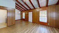 Located at 201 Audubon Dr in Danville, VA, this 2-bedroom, 1-bathroom unit offers a distinctive rustic aesthetic defined by exposed red wood beams, textured tile ceilings, and warm wood-paneled accent walls found throughout the space. Light luxury vinyl plank flooring runs continuously across the single-floor layout, providing a clean, cohesive foundation.

The combined kitchen and living area forms the heart of the unit. The living room features vaulted beam ceilings, vertical wood-panel walls, multiple windows with blinds that invite natural light, and a pendant light fixture. The kitchen is equipped with wood cabinetry, a double-basin stainless steel sink, laminate countertops, a full-size refrigerator, and hexagonal tile flooring.

Both bedrooms carry the same exposed beam ceiling detail, with wood-paneled accent walls adding warmth and character. The primary bedroom is notably spacious, featuring two windows and a window-mounted AC unit. The second bedroom includes a large window and a wood-paneled closet wall. The bathroom is straightforward, featuring a tiled tub-shower combination with white wall tile and chrome fixtures.

A hallway connects the rooms, completing this efficiently arranged and visually cohesive single-floor unit.