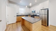 Located at 361 E 1850 S in Ogden, Utah, this contemporary three-story home offers a thoughtfully designed layout with 1 bedroom and 3 full bathrooms spread across three distinct levels. The entry level provides a welcoming foyer that flows into the main living floor, where light hardwood flooring and crisp white walls create a clean, modern aesthetic. The open-concept kitchen and living area anchors the main floor, featuring a central island with granite countertops, dual-tone cabinetry pairing white upper cabinets with warm wood lower cabinets, stainless steel appliances, and pendant lighting — ideal for both cooking and entertaining. The bathrooms echo the same design language, with wood-toned vanities topped with dark granite countertops and hardwood flooring. The upper floor houses the spacious primary bedroom, which boasts soaring ceilings, an abundance of natural light from multiple windows with views of surrounding greenery, and plush carpeting underfoot. An adjoining walk-in closet offers generous built-in shelving and hanging storage. A dedicated en-suite bathroom completes the primary suite. Throughout the home, a neutral color palette, clean lines, and consistent material choices contribute to a cohesive and modern living environment.