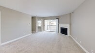 Located at 1225 Deerfield Pkwy in Buffalo Grove, IL, this well-appointed three-bedroom, two-bathroom single-floor residence offers a thoughtfully designed layout with a clean, neutral aesthetic throughout. The open-concept living and dining area is a standout, centered around a classic white-mantled fireplace and anchored by plush carpeting in warm neutral tones. Sliding glass doors lead to a private balcony, flooding the space with natural light and providing pleasant outdoor views. The kitchen features warm wood cabinetry, light quartz countertops, a double stainless steel sink, and stainless steel appliances, with light hardwood-style flooring tying the space together. A pantry adds convenient storage. The primary bedroom is generously sized and includes a dedicated en-suite bathroom. Two additional bedrooms offer comfortable carpeted spaces with ample closet access. Both bathrooms are finished with wood-look tile flooring, white vanities, and clean white fixtures. A full in-unit laundry room houses a side-by-side washer and dryer beneath abundant overhead cabinetry. With multiple closets and utility spaces, this residence delivers practical, move-in-ready living in a well-organized floor plan.