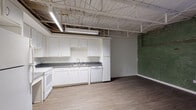 Located in Memphis, TN 38103, this one-bedroom, one-bathroom unit delivers a distinctive industrial loft aesthetic blended with practical living amenities. The open-concept living and kitchen area is anchored by an exposed ceiling featuring white-painted structural trusses, steel framing, and overhead fluorescent lighting — a hallmark of converted urban spaces. Original brick and weathered green-painted accent walls add raw, historic character throughout the main living area, providing a striking visual contrast to the clean, neutral finishes elsewhere.

The kitchen is well-equipped with white cabinetry offering ample storage, dark countertops, a stainless steel sink, a full-size refrigerator, electric range with oven, dishwasher, and microwave. Light wood-tone vinyl plank flooring runs through the kitchen and living area, transitioning to darker hardwood tones in the bedroom zone. A window with shutters allows natural light to filter into the living space.

The bedroom features the same exposed brick accent wall and a standard entry door. The full bathroom is spacious and accessibility-friendly, outfitted with ADA-compliant grab bars, a vanity with dark countertop, tile flooring, and clean white walls. This unit is ideal for those seeking urban character in the heart of Memphis.
