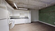 Located in Memphis, TN 38103, this one-bedroom, one-bathroom unit delivers a distinctive industrial loft aesthetic blended with practical living amenities. The open-concept living and kitchen area is anchored by an exposed ceiling featuring white-painted structural trusses, steel framing, and overhead fluorescent lighting — a hallmark of converted urban spaces. Original brick and weathered green-painted accent walls add raw, historic character throughout the main living area, providing a striking visual contrast to the clean, neutral finishes elsewhere.

The kitchen is well-equipped with white cabinetry offering ample storage, dark countertops, a stainless steel sink, a full-size refrigerator, electric range with oven, dishwasher, and microwave. Light wood-tone vinyl plank flooring runs through the kitchen and living area, transitioning to darker hardwood tones in the bedroom zone. A window with shutters allows natural light to filter into the living space.

The bedroom features the same exposed brick accent wall and a standard entry door. The full bathroom is spacious and accessibility-friendly, outfitted with ADA-compliant grab bars, a vanity with dark countertop, tile flooring, and clean white walls. This unit is ideal for those seeking urban character in the heart of Memphis.