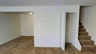 Located at 1204 Kitmore, this two-floor residence presents a straightforward and functional interior design. The space is finished with wall-to-wall carpeting in a warm tan tone, creating a soft underfoot feel throughout the living areas. Crisp white walls provide a neutral backdrop, contributing to a clean and bright atmosphere.

The image reveals a carpeted room featuring an open bifold closet door, exposing a built-in shelving and hanging rod system that offers practical storage solutions. An adjacent room is visible through an open doorway, illuminated by a flush-mount ceiling light fixture, suggesting a connected and open flow between spaces. Light switches, a thermostat panel, and electrical outlets are conveniently placed along the walls.

The overall aesthetic is simple and unadorned, prioritizing utility and ease of use. The two-floor layout provides separation between living and private spaces, adding functionality to the home. The neutral color palette and carpeted floors throughout give the residence a calm, livable ambiance suitable for a variety of furnishing styles.