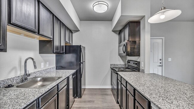 Disfrute de encimeras de granito, fregaderos de acero inoxidable y electrodomésticos negros. - Sendero Ridge Apartments