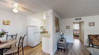 This single-floor unit offers a practical and functional layout across several well-defined living areas. The kitchen is designed in a galley style, featuring white cabinetry, warm-toned laminate countertops, wood-look vinyl flooring, a white electric range, and a full-size refrigerator. A half-wall partition separates the kitchen from the adjoining dining and living spaces, creating an open yet organized flow throughout the unit. The dining area accommodates a small table and benefits from natural light through a vertical-blind-covered window. The living room continues the open feel, finished with neutral carpet, a window allowing natural light, and a closet for additional storage. The bedroom is a quiet, carpeted retreat with a window fitted with vertical blinds and a walk-in closet equipped with a hanging rod and shelf. The bathroom includes wood-look vinyl flooring, a tub and shower combination with stone-patterned surround, and a standard toilet. Textured ceilings are consistent throughout the unit, contributing to its cohesive, understated aesthetic.