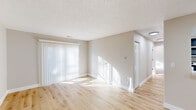 This single-floor unit presents a clean, modern aesthetic defined by a neutral color palette, crisp white trim, and textured ceilings throughout. The main living area is generously sized, featuring light-toned hardwood flooring that extends throughout the common spaces, and large sliding glass doors dressed with vertical blinds that flood the room with natural light. Adjacent to the living area, a pass-through counter connects to the kitchen, which is outfitted with dark espresso cabinetry, light countertops, and a full suite of stainless steel appliances including a refrigerator, electric range, and over-the-range microwave. Recessed lighting and a pendant fixture illuminate the dining and kitchen transition area. The bedrooms are carpeted for comfort, each offering ample wall space and closet access. One bedroom features a window with horizontal blinds, inviting natural light into the room. The bathrooms maintain the unit's clean aesthetic, with a white vanity, chrome fixtures, a well-lit mirror, and a tiled shower-tub combination. Throughout the space, consistent neutral wall tones and white baseboards contribute to a cohesive, move-in-ready environment that is both functional and inviting.