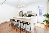 This 450 square foot apartment in Montréal offers a thoughtful blend of style and functionality. The open-concept kitchen and living area is the heart of the home, showcasing sleek white cabinetry, stainless steel appliances, and a central island that doubles as a dining space. Four pendant lights above the island add a touch of modern elegance.

The kitchen is fully equipped with a range, refrigerator, and cleverly integrated stackable washer and dryer units, maximizing the use of space. Warm wood-look flooring throughout creates a cohesive feel and adds warmth to the crisp white walls and cabinetry.

The bedroom, measuring 130 square feet, features a large window allowing natural light to flood the space. The bathroom is efficiently designed with a white vanity, glass-enclosed shower, and modern fixtures.

Large windows in the living area and a glass-paned door leading to a balcony invite ample natural light, creating an airy atmosphere. The apartment's layout, while compact, feels spacious due to its open design and clever use of vertical space.

This urban dwelling combines contemporary design with practical living, ideal for those seeking a modern, low-maintenance lifestyle in the heart of Montréal.
