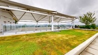Located in Vancouver's Mount Pleasant neighbourhood, this rooftop terrace at 333 E 11th Ave offers a thoughtfully designed outdoor amenity space with a wide variety of functional zones. The terrace is defined by its striking tensile fabric canopy structures, which provide sheltered areas for both lounging and outdoor dining. Beneath the canopies, modern white patio furniture and a built-in barbecue station create a well-equipped gathering space ideal for social events.

Lush green roof sections run along the perimeter, featuring maintained turf and ornamental plantings that add a naturalistic quality to the rooftop environment. Wide concrete pathways connect the various zones, bordered by glass and metal railings that preserve sweeping panoramic views of the Vancouver skyline, surrounding neighbourhoods, and distant mountains.

A dedicated children's play area features colourful rubber safety flooring in a checkerboard pattern alongside climbing structures, making the terrace a versatile space for all ages. Walkways overlooking an interior atrium below provide additional visual interest and connectivity throughout the level.

The open-air design maximizes exposure to the surrounding cityscape while the canopy structures ensure usability regardless of weather, making this rooftop terrace a highly functional and visually engaging amenity.