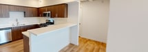 Located at 23742 Washington Avenue in Murrieta, CA, this thoughtfully designed 1-bedroom, 1-bathroom residence offers a clean, contemporary aesthetic throughout its well-utilized single-floor layout. Light wood-tone flooring flows consistently through every room, complementing the crisp white walls and creating a bright, cohesive atmosphere.

The open-concept living, dining, and kitchen area serves as the heart of the home. The kitchen is outfitted with rich walnut-toned cabinetry, white quartz countertops, a full suite of stainless steel appliances including a gas range, microwave, dishwasher, and refrigerator, and a peninsula that provides additional prep and dining space. Recessed lighting illuminates the area effectively.

The bedroom is a well-proportioned retreat featuring a window with blinds that invites natural light. It connects to a dedicated walk-in closet with built-in shelving, providing ample storage. A second closet adds further organizational flexibility. The full bathroom mirrors the modern finishes seen throughout, featuring a single-sink vanity with walnut cabinetry, quartz countertop, a large mirror, and a soaking tub with a built-in niche. An in-unit laundry area adds everyday convenience. The private balcony offers an outdoor retreat with open-sky views.