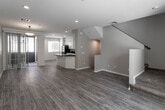 Located at 1235 Doris Ln in Corona, California, this three-story home offers a well-organized multi-level layout designed for comfortable everyday living. The ground floor includes a spacious attached garage with an automatic opener, providing ample room for vehicles and storage. The main living level features an open-concept layout where the living and dining areas flow seamlessly together. Sliding glass doors lead to a private outdoor balcony, filling the space with natural light. The kitchen is equipped with crisp white shaker cabinetry, dark granite countertops, black appliances including a gas range and built-in microwave, and light wood-style flooring that extends throughout the main living area. The staircase, accented by warm wood handrails and carpet treads, connects each floor efficiently. Hallways on the upper levels feature hardwood-style flooring alongside carpeted bedrooms. Bathrooms are finished with warm wood-toned cabinetry, stone-style countertops, large mirrors, and tub-shower combinations. The primary bathroom includes a double-sink vanity and convenient access to a walk-in closet. Bedrooms are carpeted and offer access to private balconies with views of the surrounding neighborhood, adding an airy, open feel to the upper floors.