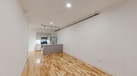 Located at 230 Goldsboro St S in Wilson, NC, this one-bedroom, one-bathroom loft blends industrial character with modern finishes throughout its well-appointed single floor. The open-concept living and kitchen area features warm hardwood floors, crisp white walls, and recessed and track lighting overhead, creating a bright and functional space. The kitchen is equipped with stainless steel appliances, including a microwave, range, and refrigerator, complemented by gray cabinetry and an island with a peninsula countertop — ideal for both cooking and casual dining. The generously sized bedroom showcases soaring ceilings, exposed brick walls, a rustic wooden structural column, and a large window that invites natural light and outdoor views. Industrial-style exposed conduit adds to the loft's character. A dedicated closet features built-in wire shelving for ample storage. The bathroom offers a clean, classic aesthetic with penny tile flooring, a full tub-shower combination, a vanity, and chrome fixtures. A staircase is also part of the layout, adding to the vertical dimension of this distinctive urban residence.
